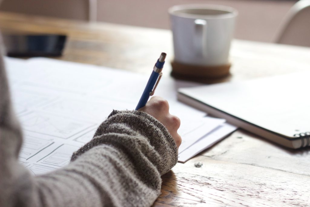 A photograph of the hand of a person drawing a page layout on a large piece of paper.